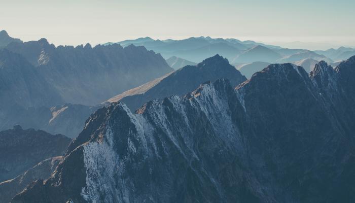 Steep, snowy mountains with a hazy blue sky above them.